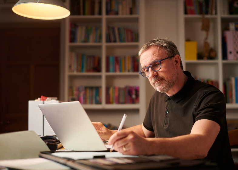 Man learning on a laptop while taking handwritten notes in a notebook